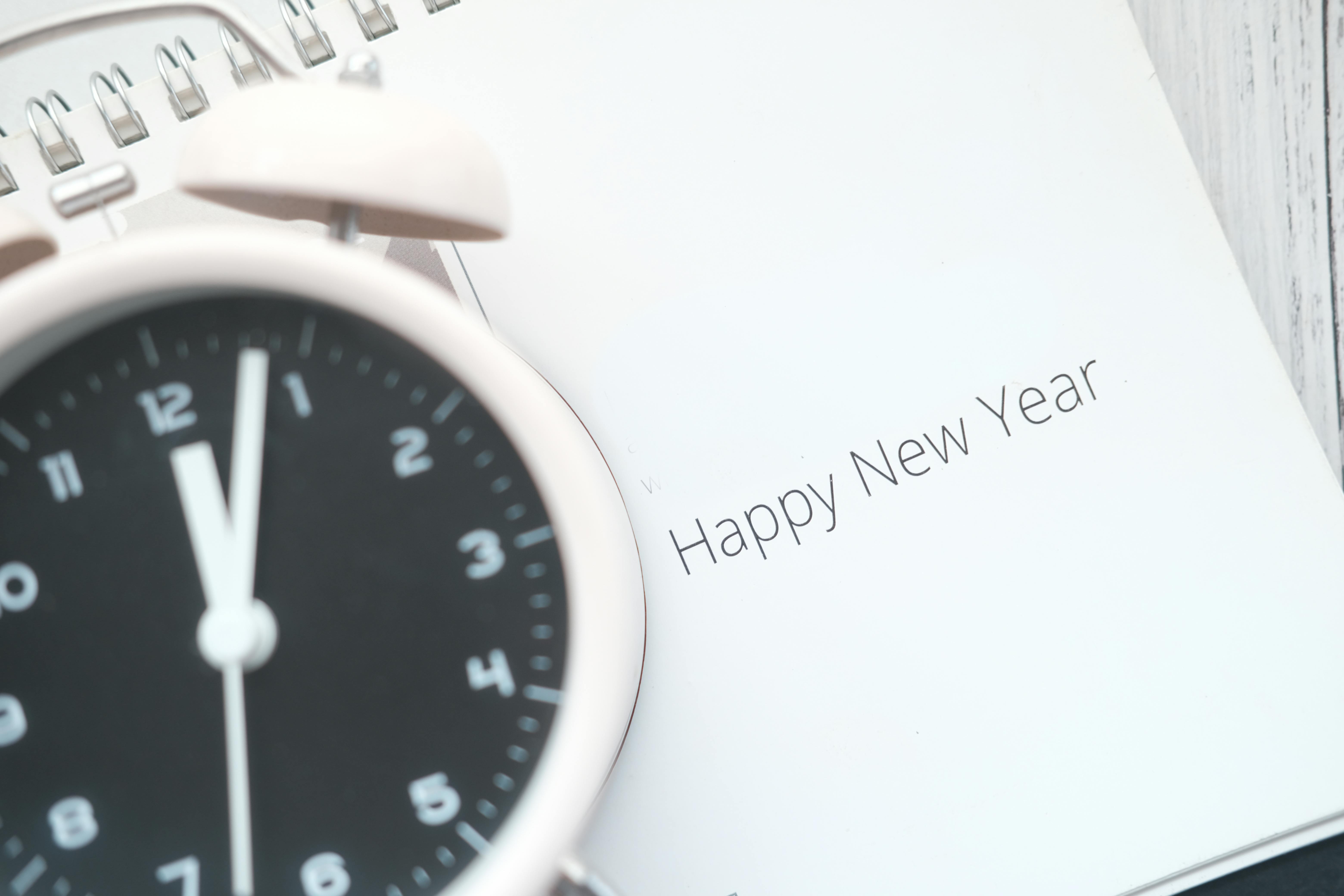 A close-up of an analog alarm clock and a 'Happy New Year' note, symbolizing the countdown to the new year.