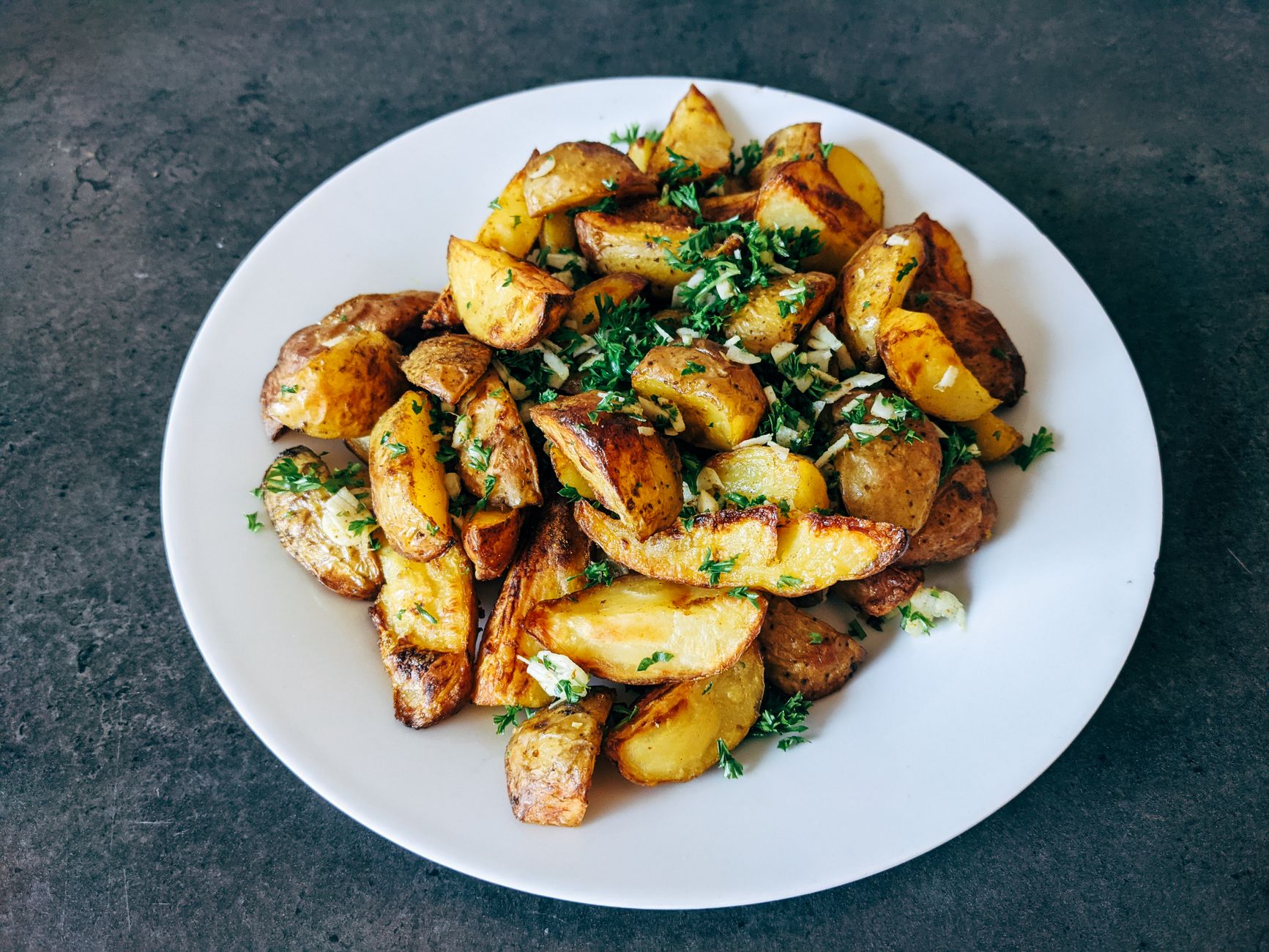 Bowl of crispy garlic roasted potatoes garnished with parsley