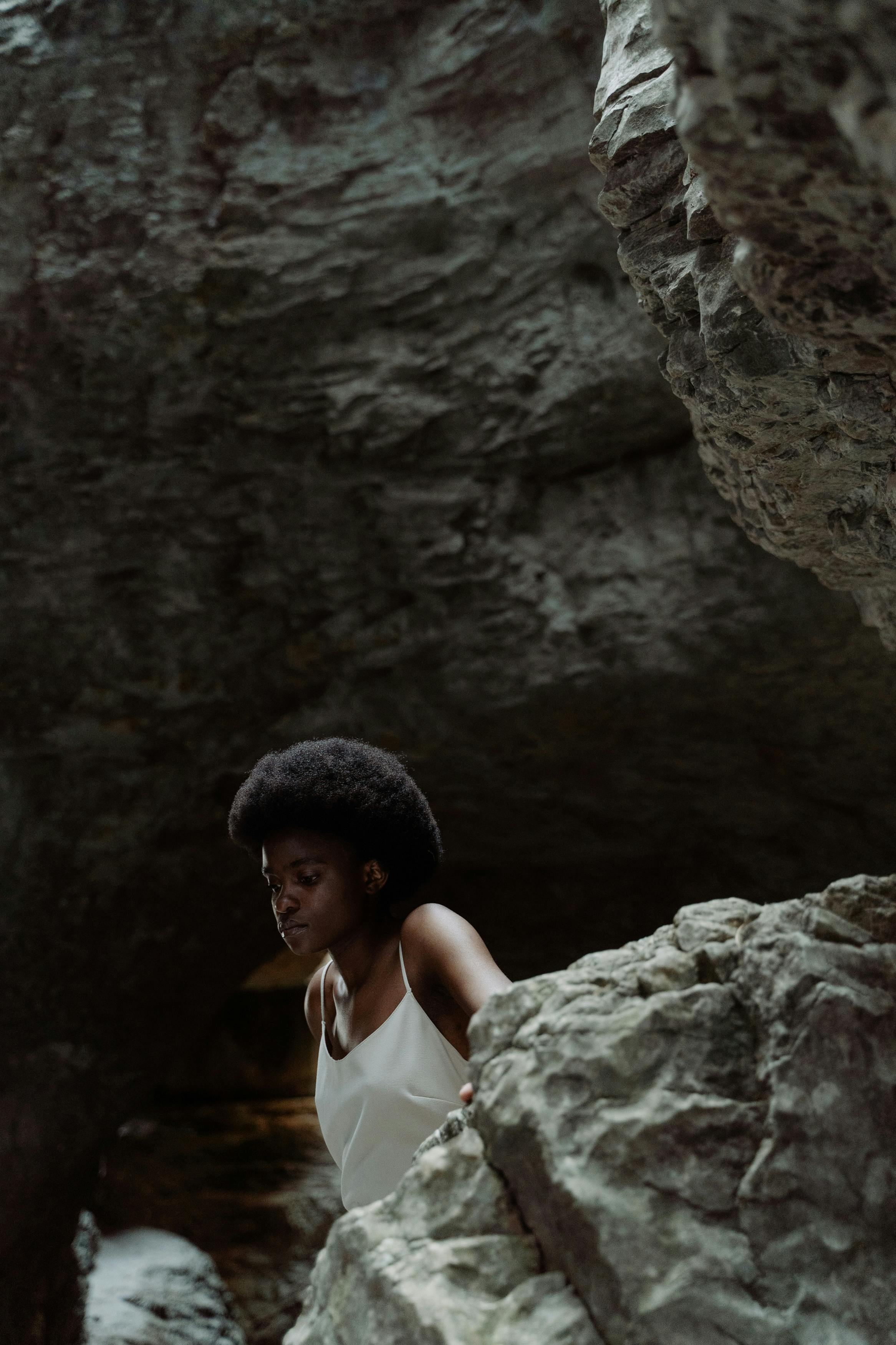 An artistic portrait of a black woman posing thoughtfully inside a rugged cave.