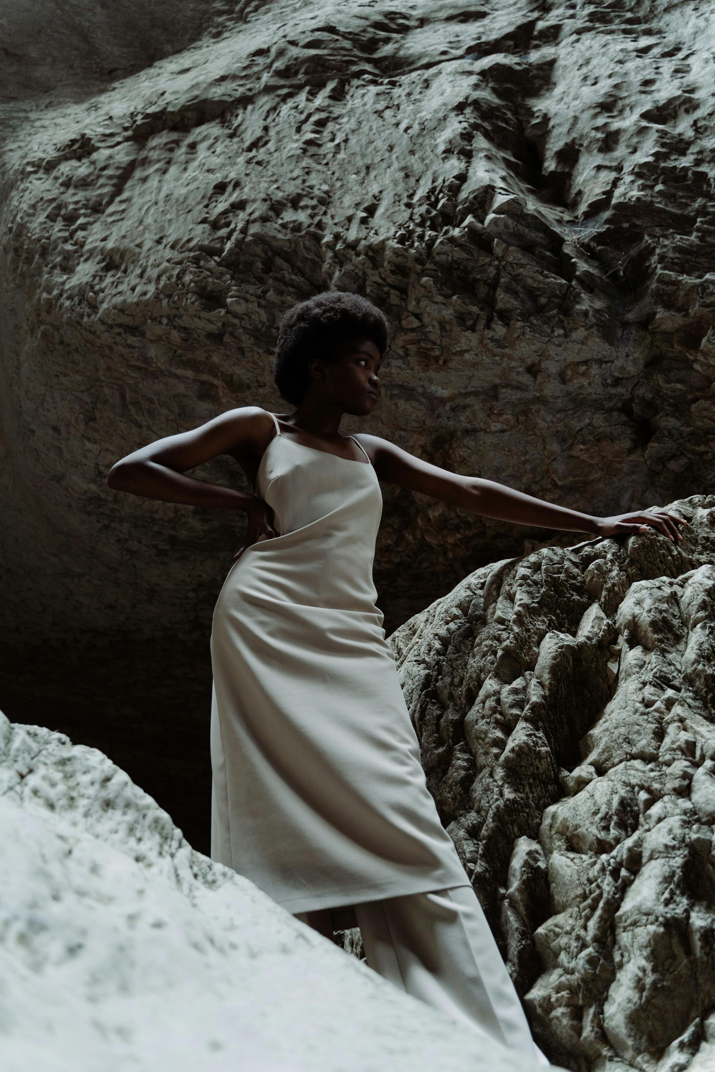 Striking portrait of a woman in a stylish dress, standing amidst a cavern's rock formations.