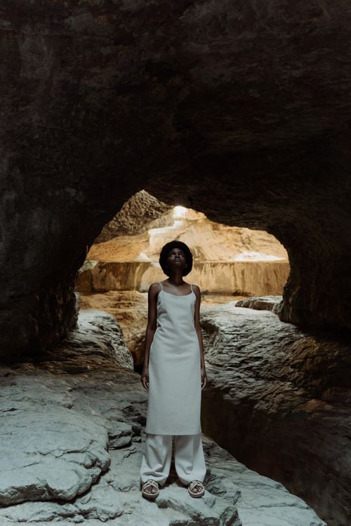 Free Fashionable woman standing confidently in a rocky cave, showcasing unique style and elegance. Stock Photo