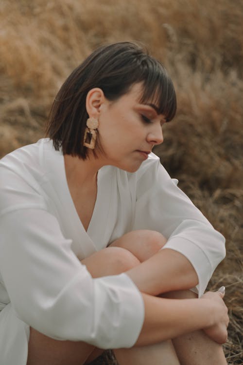 Woman in White Long Sleeves Sitting on Brown Grass 