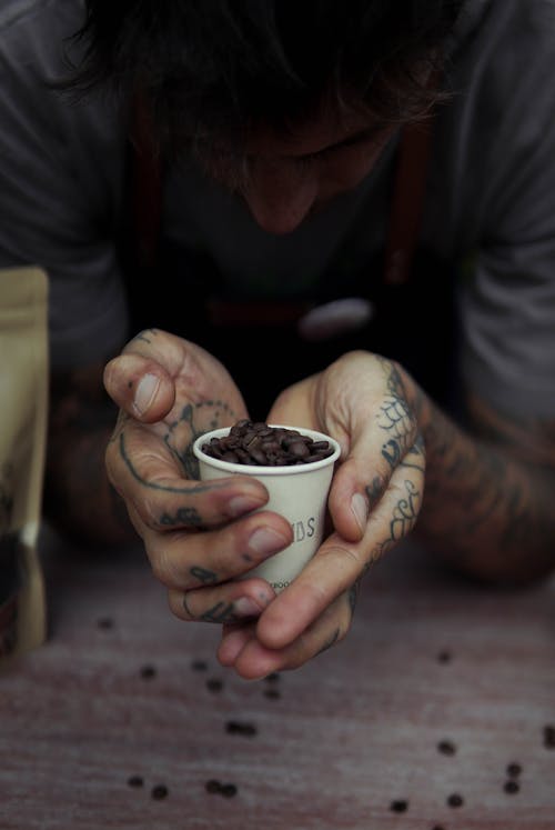 A Tattooed Man Holding a Paper Cup with Coffee Beans