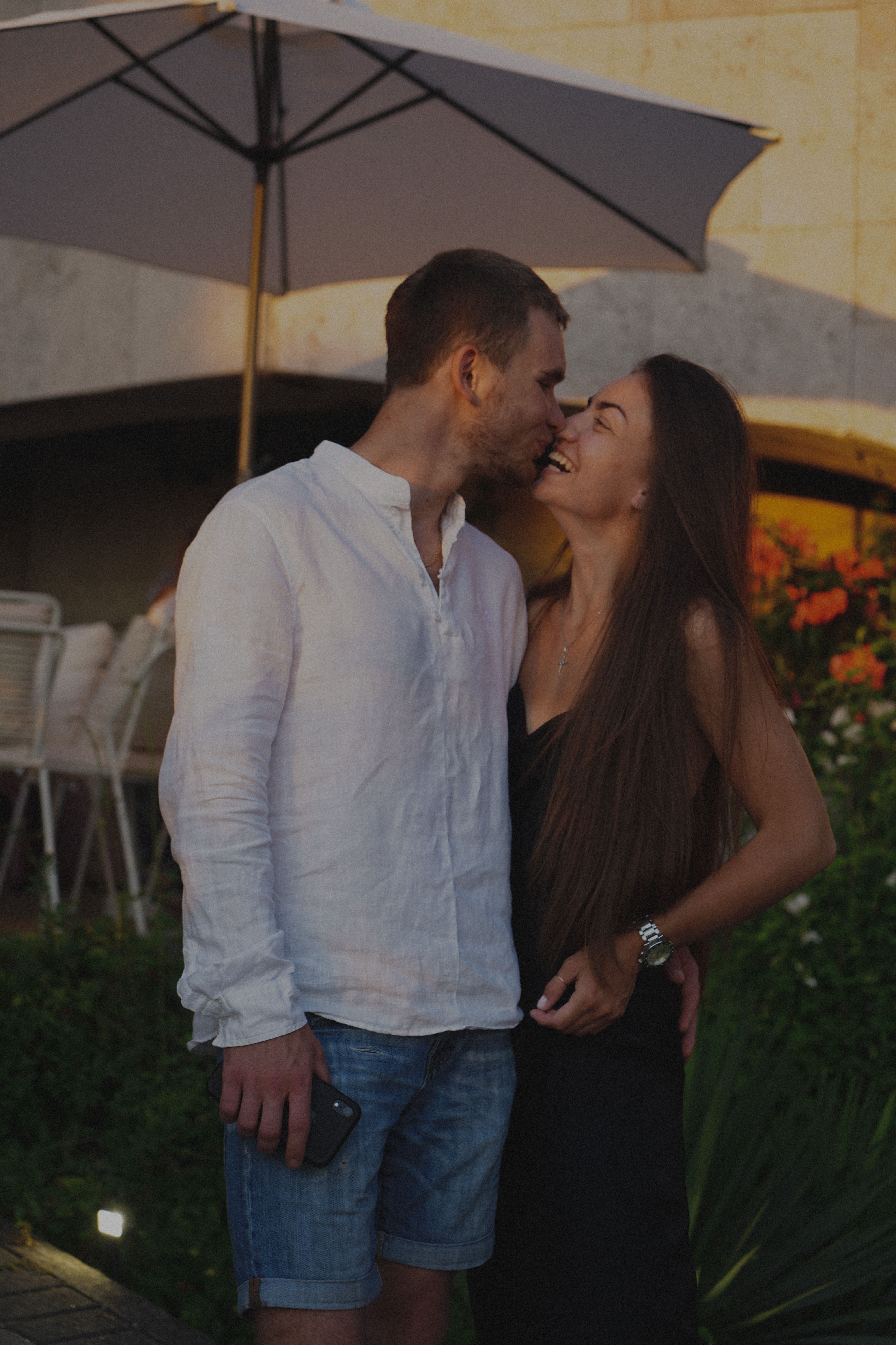 A loving couple embracing and smiling outdoors under a patio umbrella.