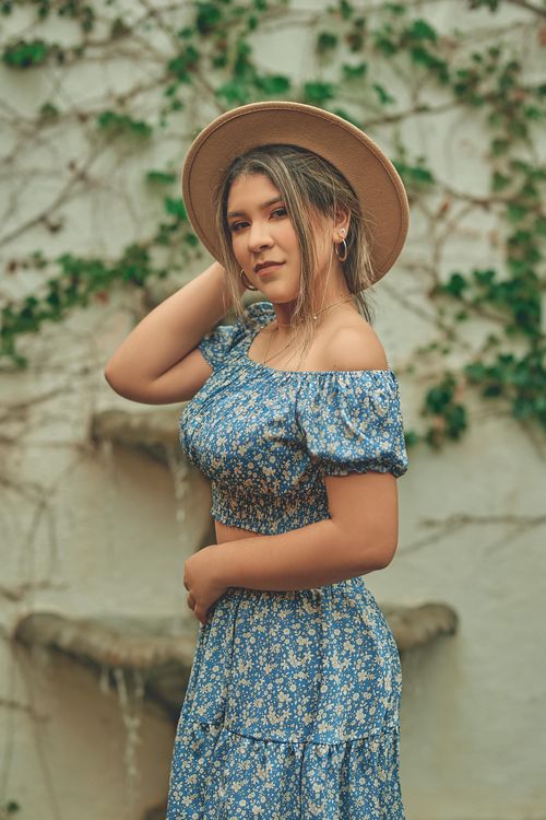 Free Chic woman posing outdoors in a floral dress and hat, exuding summer elegance. Stock Photo