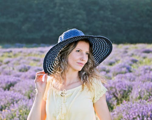 A Woman in Yellow Shirt Wearing a Hat while Standing on a Flower Field