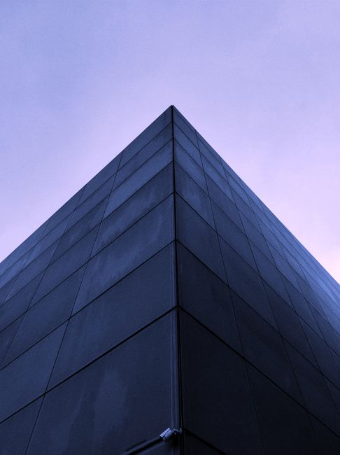 Low angle view of a sleek modern building facade against a purple twilight sky.