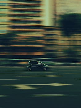 A compact car speeds down a city street captured in a motion-blur effect, conveying speed and movement.
