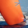 A sailboat with a bright orange spinnaker sail catches the wind as it cuts through the water.