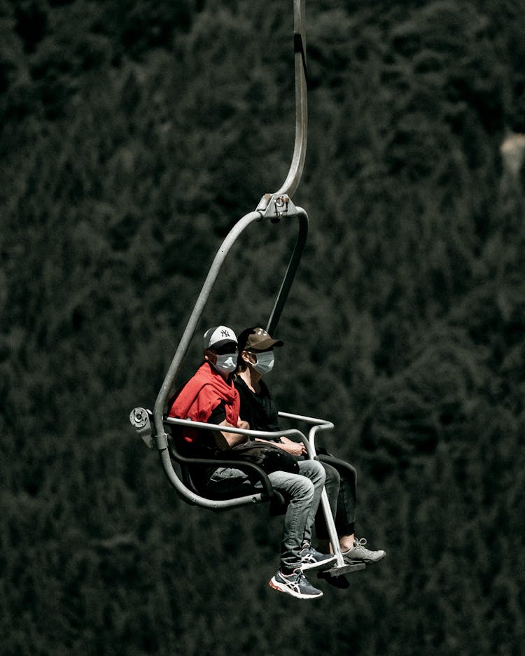 People In Face Masks Riding On Hoist Above Forest