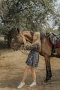 Woman in Blue and White Plaid Skirt Standing Beside Brown Horse