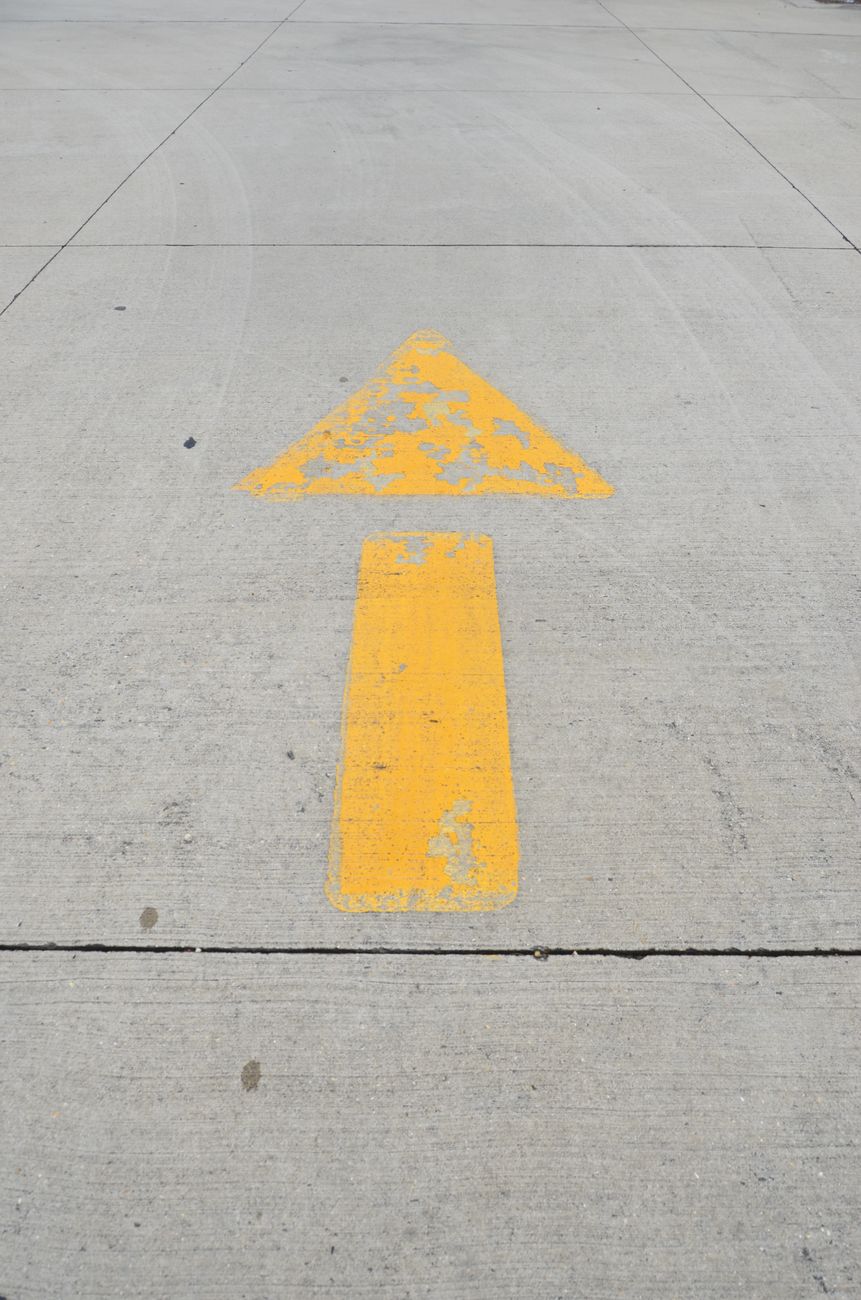 A weathered yellow arrow on concrete pavement directs traffic in an urban setting.