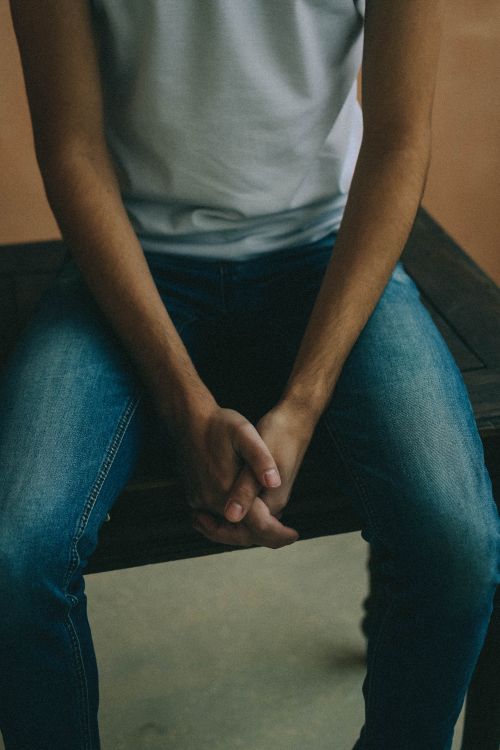 Free Person sitting casually with hands together, wearing denim pants and white shirt. Stock Photo