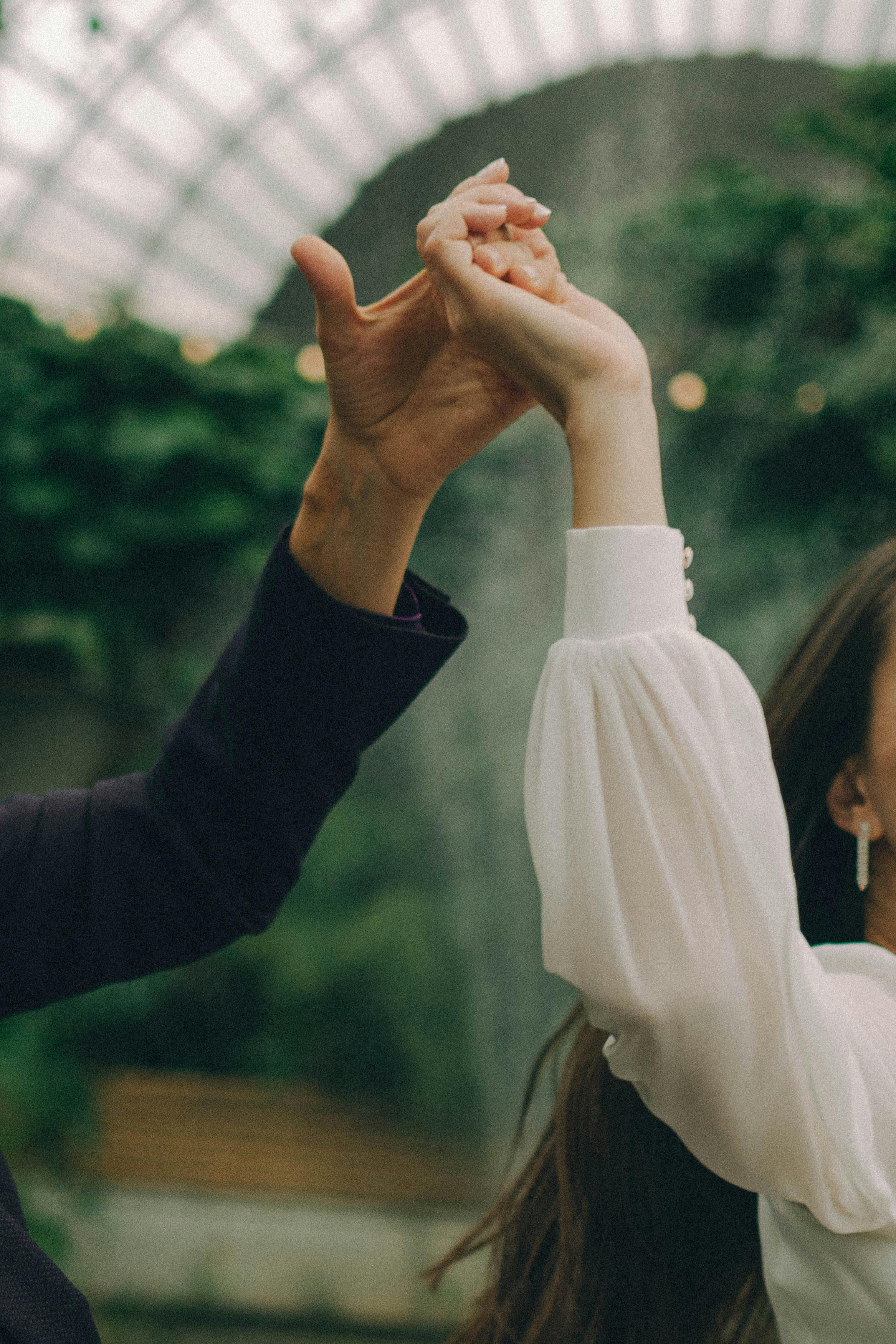 A close-up of two people holding hands elegantly indoors, sunlight filtering through.