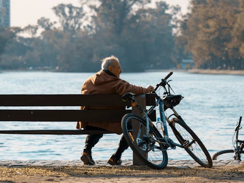 Free Man Sitting on the Wooden Bench Beside His Bicycle  Stock Photo