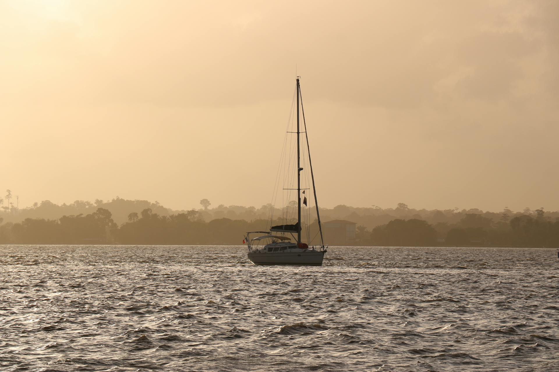 A serene sailboat drifting on the ocean against a warm sunset in French Guiana.