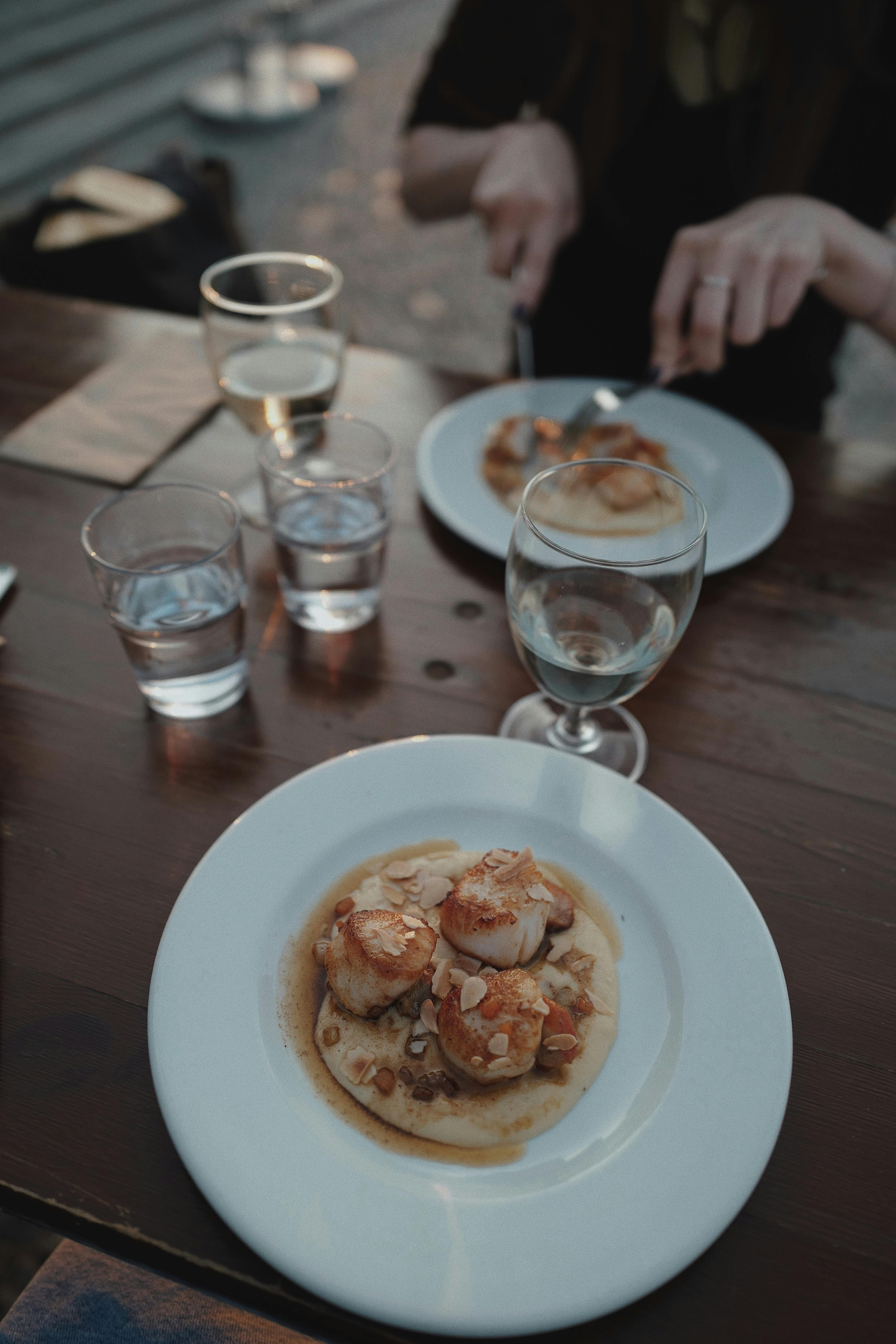 Gourmet scallops artfully plated on a wooden table setting in a cozy restaurant atmosphere.