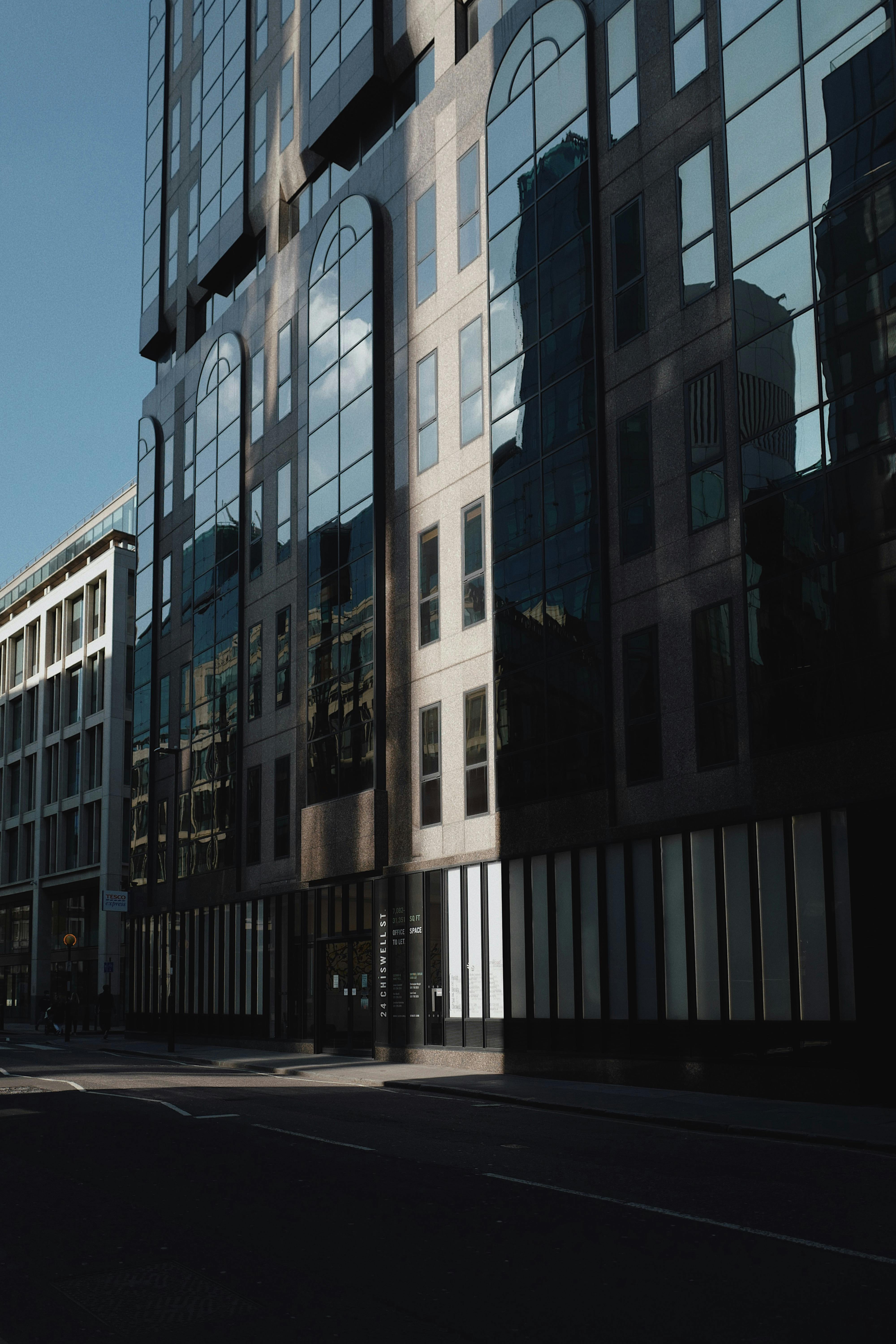 A low angle view of a modern glass building with reflective windows on a city street.