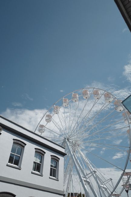Low angle view of a Ferris wheel near a building under a clear blue sky.