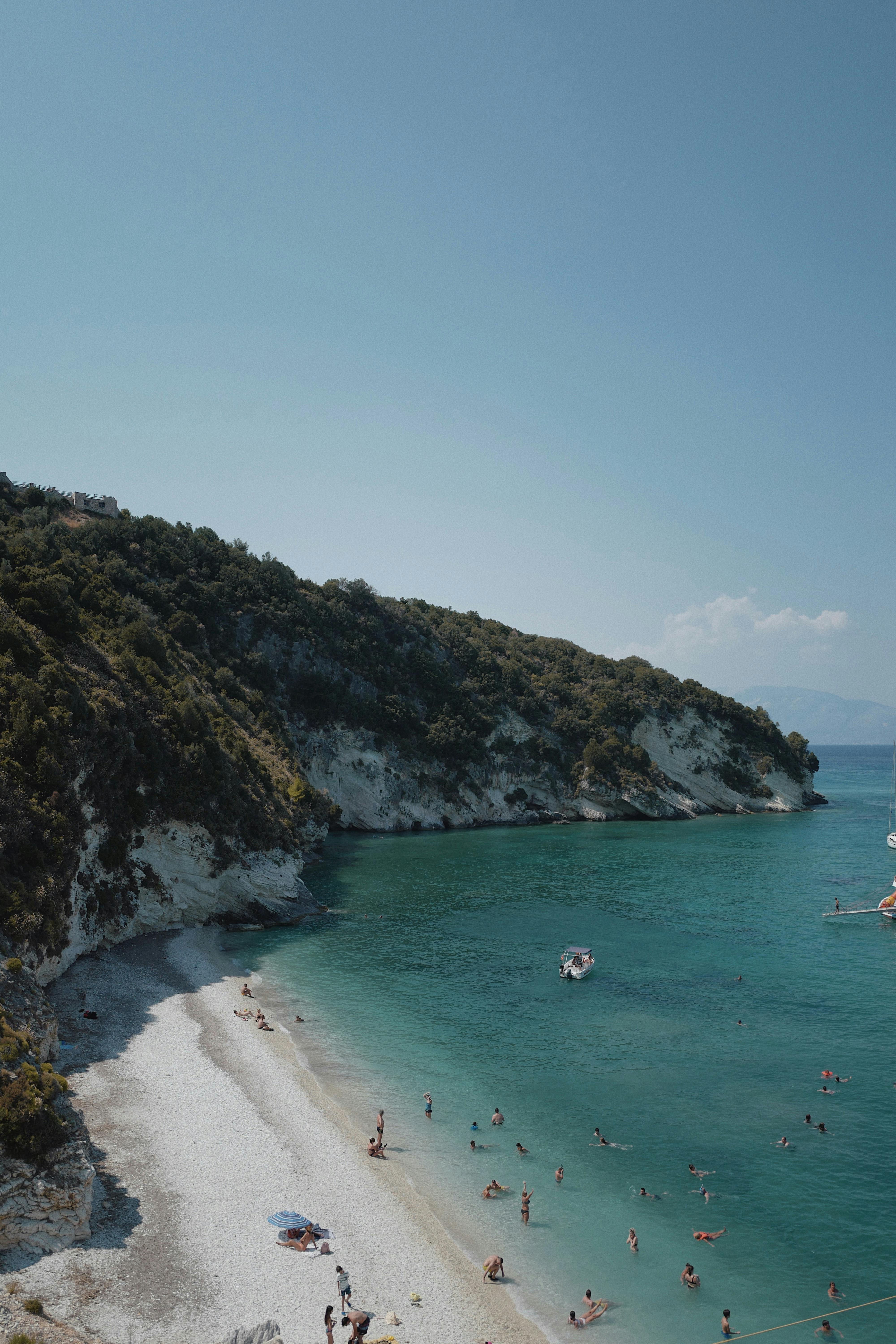 A breathtaking aerial view of a rocky beach with people swimming and relaxing in the turquoise sea.