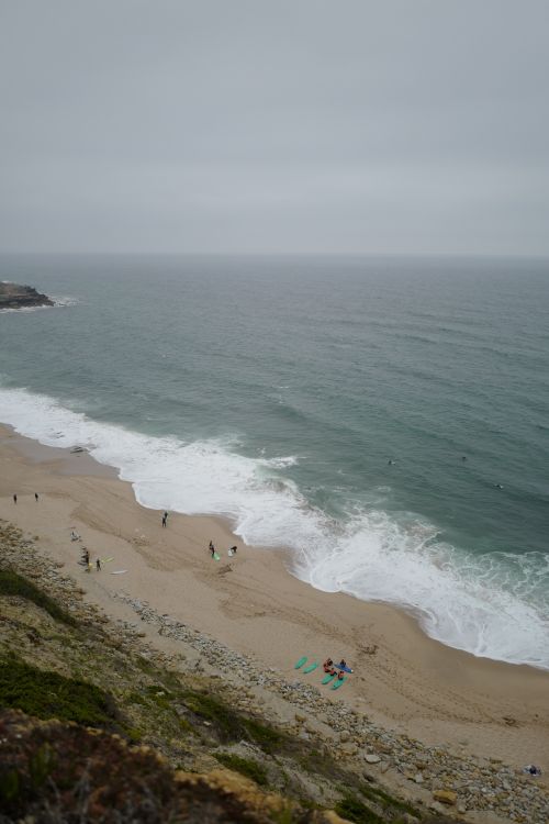 Free A scenic aerial view of a sandy beach with crashing waves and scattered people relaxing. Stock Photo