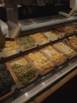 A variety of fresh uncooked pastas in a market display, showcasing different colors and shapes.