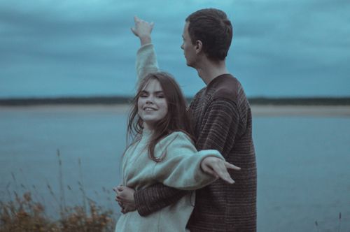 Free Young couple sharing a joyful embrace by the lake under a cloudy sky. Stock Photo