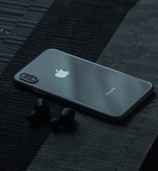 A sleek smartphone and wireless earphones displayed on a dark textured surface, showcasing modern technology.