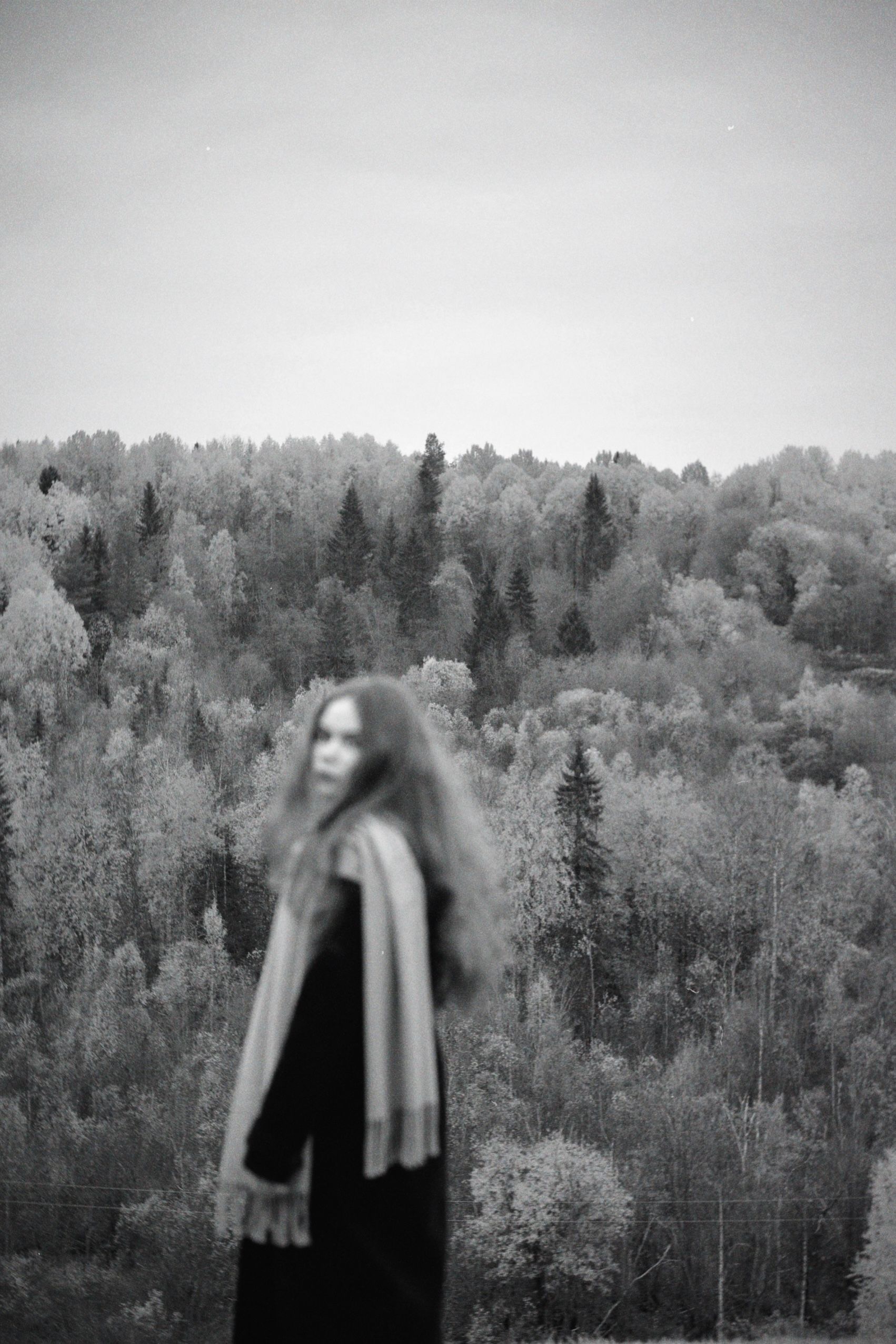 Blurry portrait of a woman in a scarf and coat with a forest backdrop.