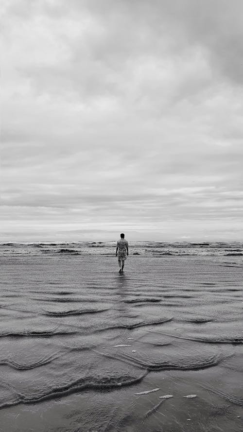 Black and White Photo of Person Walking on Shore