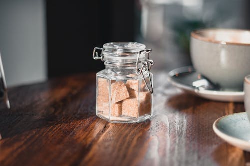 бесплатная Прозрачный шейкер для приправ с кубиками коричневого сахара возле серой чашки Стоковое фото