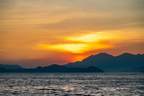 Free Stunning ocean view with vibrant sunset colors and mountain silhouettes, capturing nature's beauty. Stock Photo