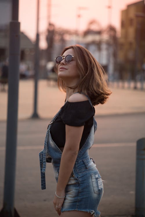 A Woman in Denim Jumper and Sunglasses Standing on the Street