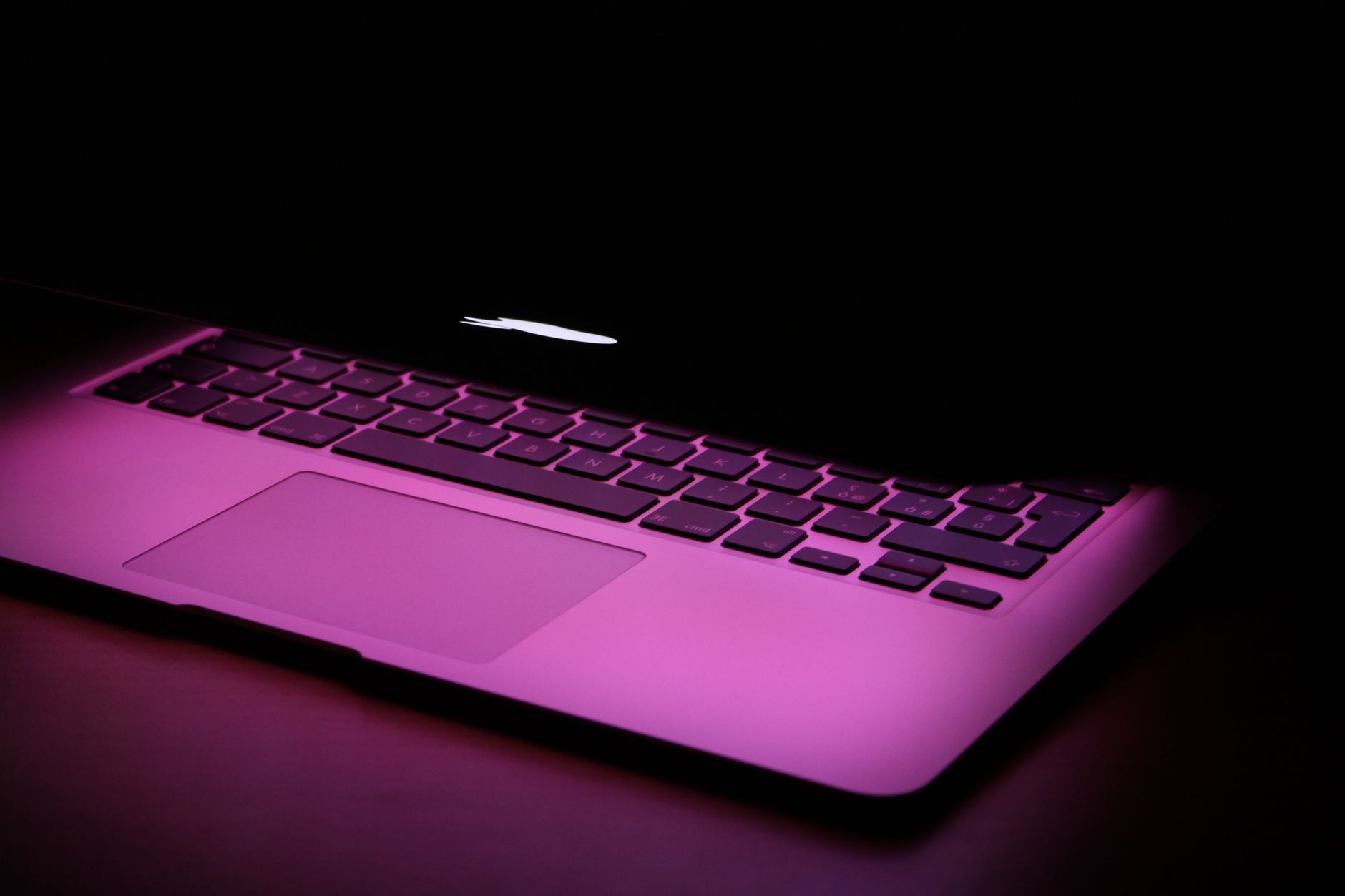 A stylish laptop partially closed, illuminated by a pink light, highlighting its modern design.