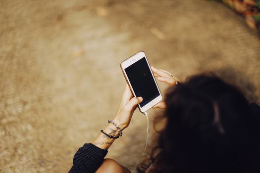 A woman holding a smartphone with headphones outdoors, perfect for technology and lifestyle concepts.