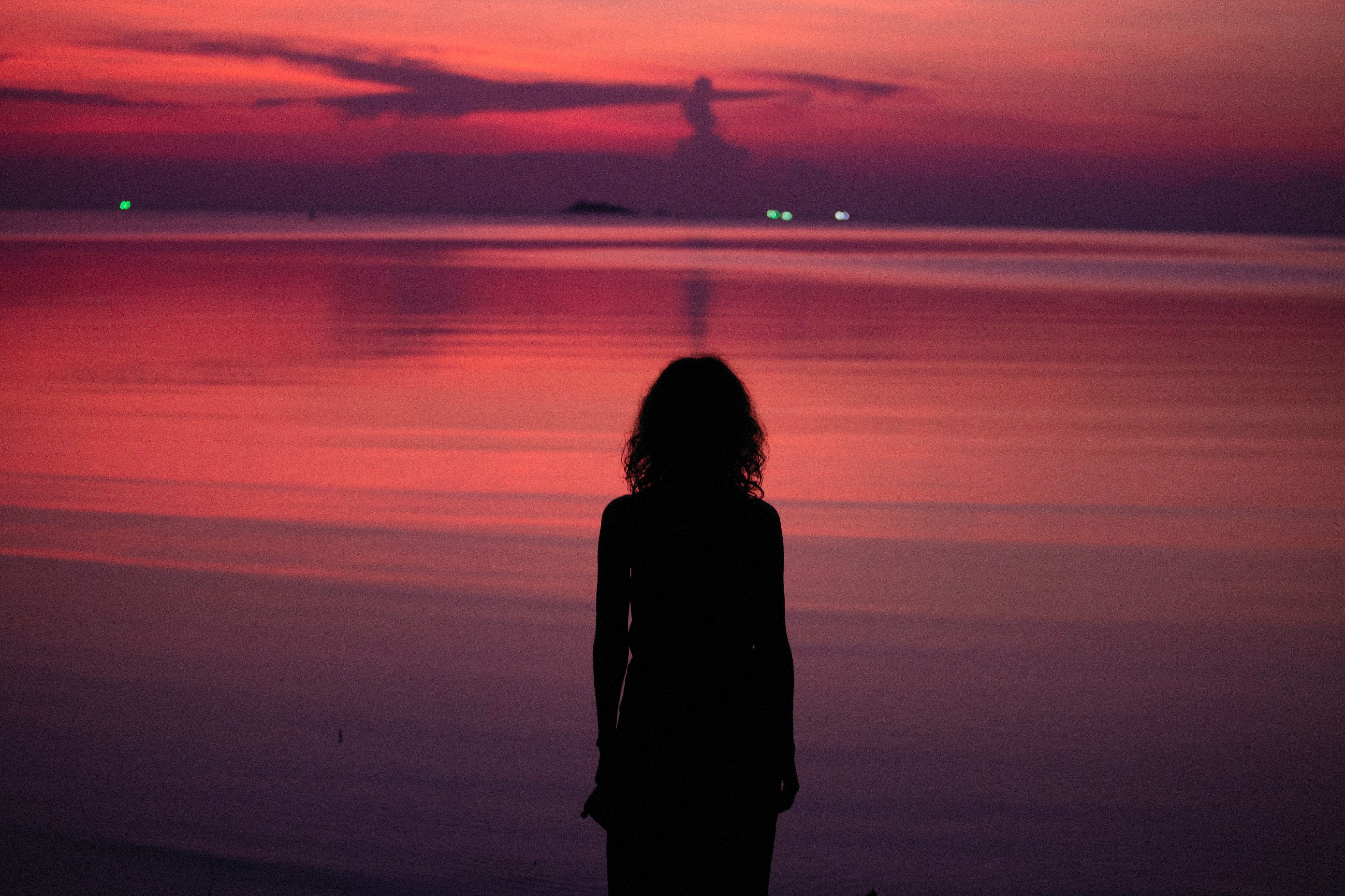 Silhouette of a Woman Standing on Beach during Sunset · Free Stock Photo