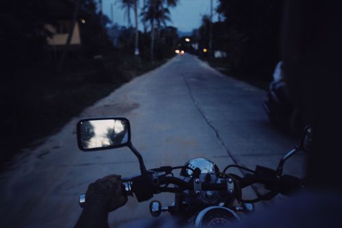 Free Motorcyclist riding down a rural road at dusk, capturing reflections in the side mirror. Stock Photo