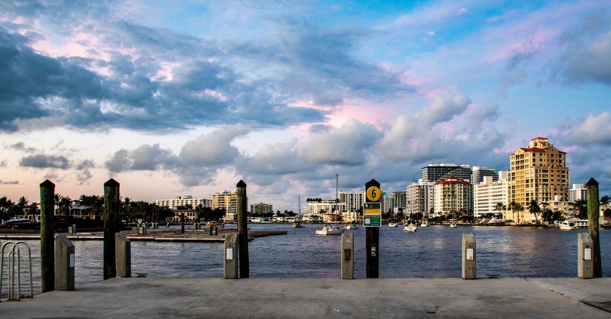 Scenic view of a vibrant waterfront city skyline at sunset with boats and clouds.