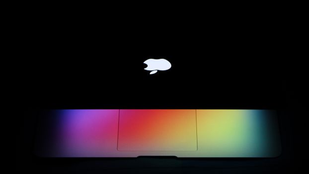 A MacBook Air with a vibrant rainbow effect on the keyboard under dark lighting showcases modern technology aesthetics.