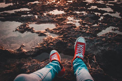 Free Person in red sneakers relaxing on a rocky shoreline at sunset, creating a serene outdoor scene. Stock Photo