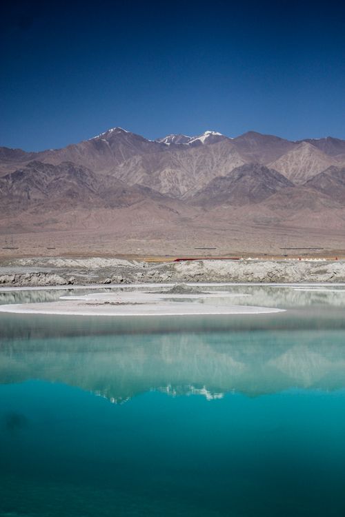 Free A serene mountain landscape reflected in a calm turquoise lake under a clear blue sky. Stock Photo