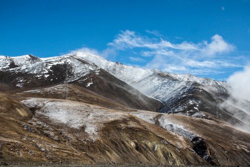 Free Majestic snow-capped mountains with a clear blue sky and scattered clouds create a stunning winter landscape. Stock Photo