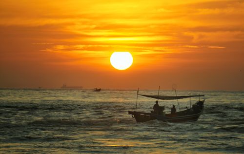 Free A fishing boat silhouetted against a vibrant sunset over a tranquil sea, capturing the essence of peaceful maritime life. Stock Photo