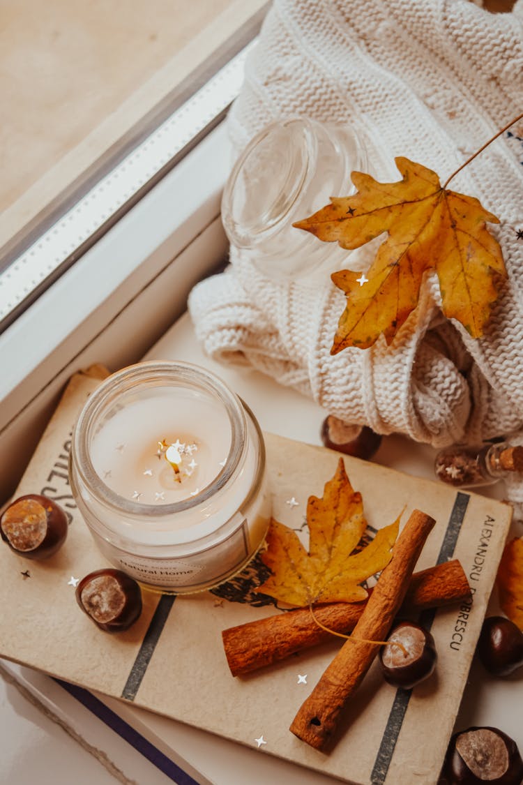 Top View Of A Candle Beside Cinnamon Sticks And Maple Leaves