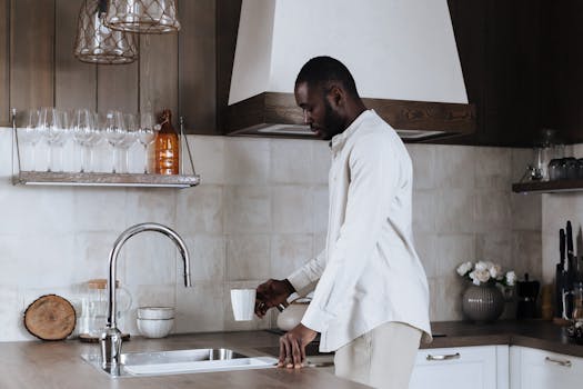 A man stands at the kitchen sink preparing a coffee cup in a modern home interior.