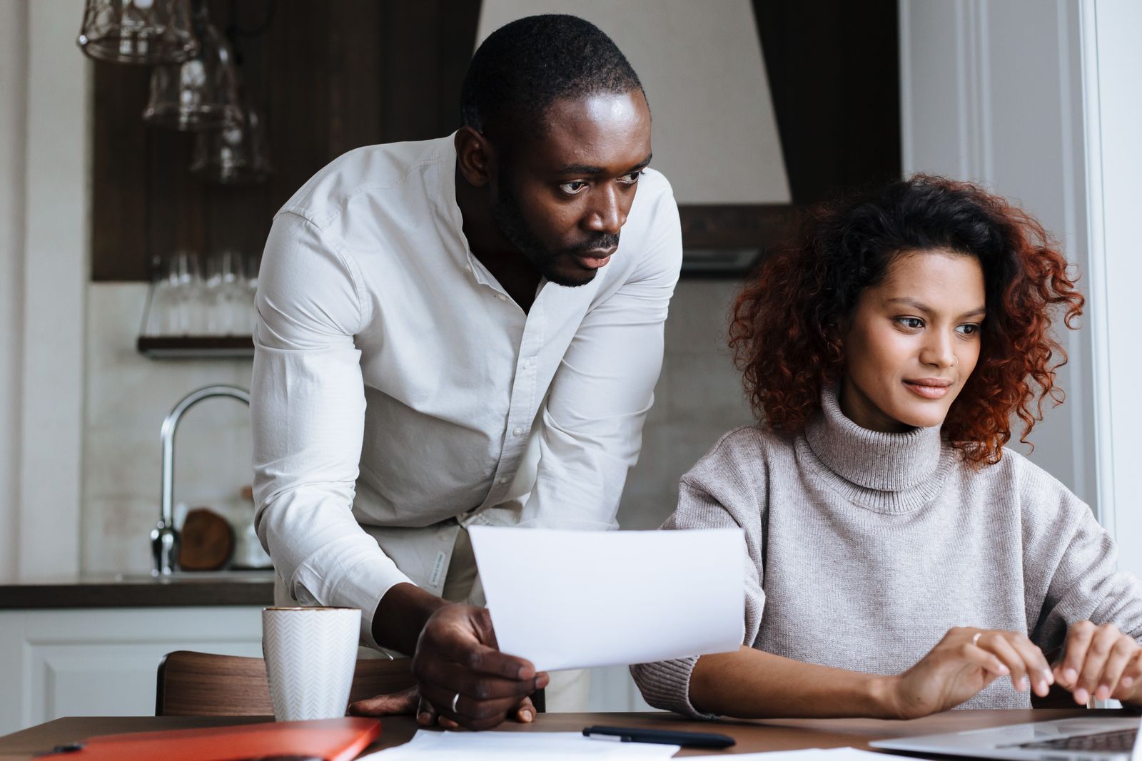 A couple reviewing paperwork together on a laptop at a kitchen counter