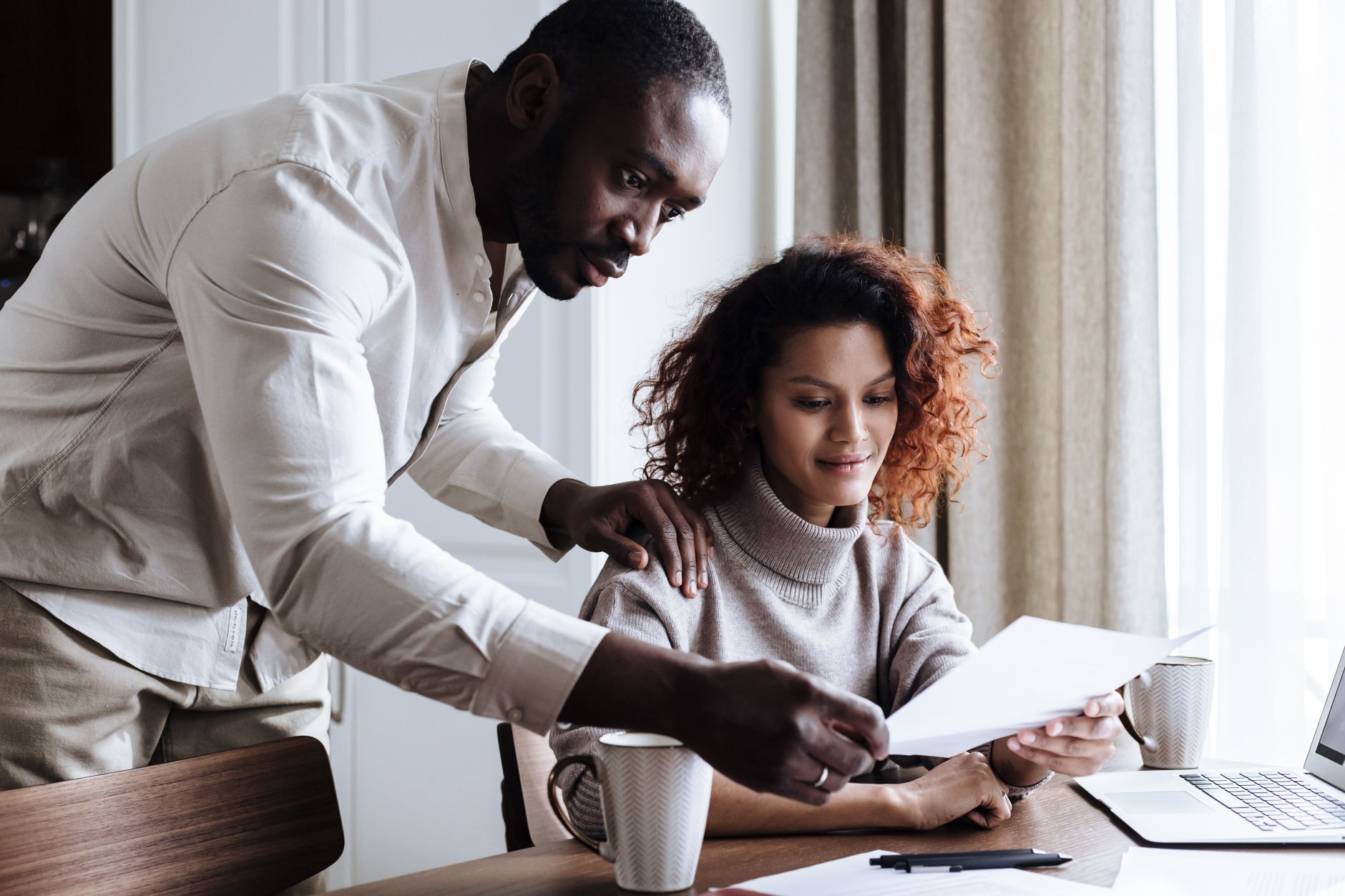 A couple working together at home, reviewing documents with a laptop and coffee.