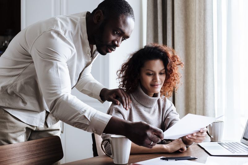 A couple working together at home, reviewing documents with a laptop and coffee.