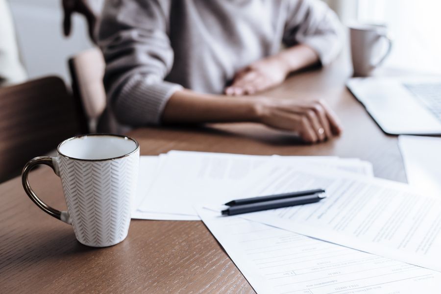 A person at a table with rental paperwork, a pen, and a coffee mug