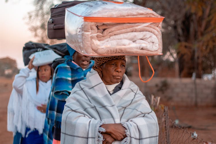 Woman Carrying A Plastic Bag With Folded Comforter On Her Head